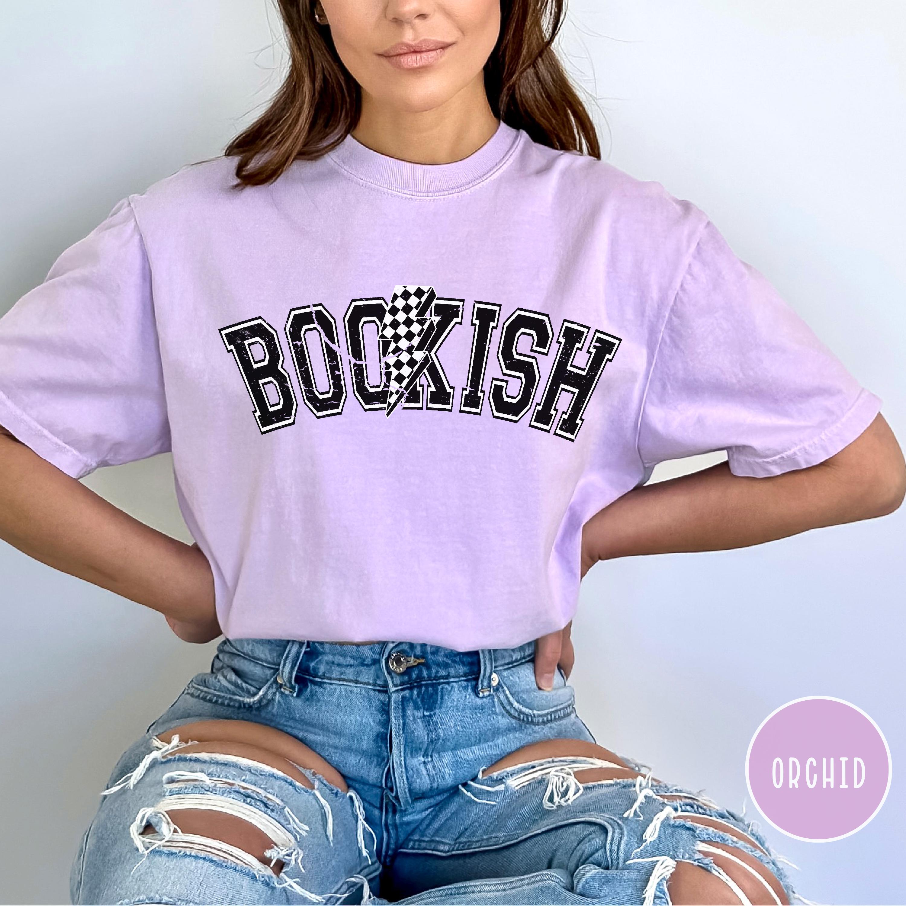A person wearing a purple oversized t-shirt with the word 'BOOKISH' printed on the front in bold letters, paired with ripped jeans.