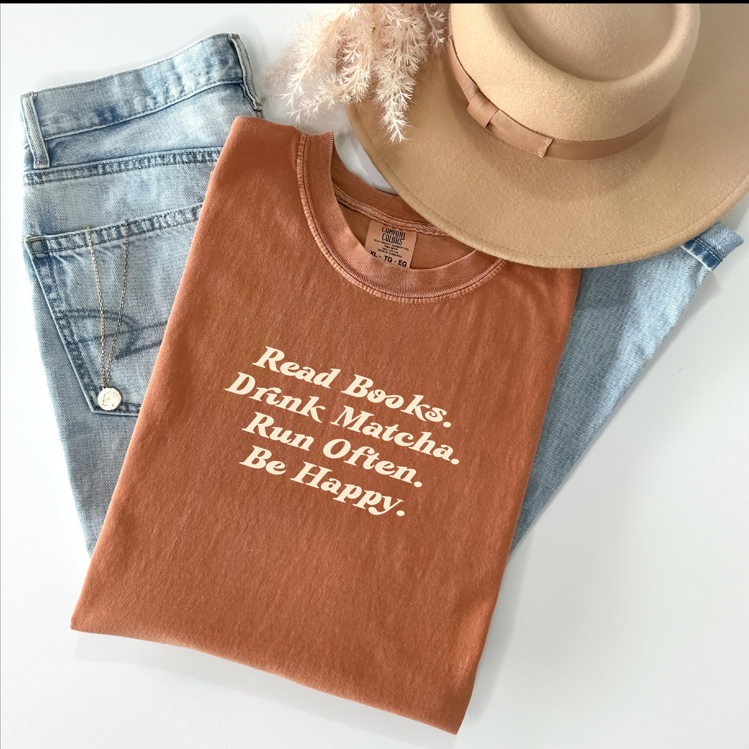 Read Books Drink Matcha Run Often Be Happy tee in Yam, styled with books and cozy props.
