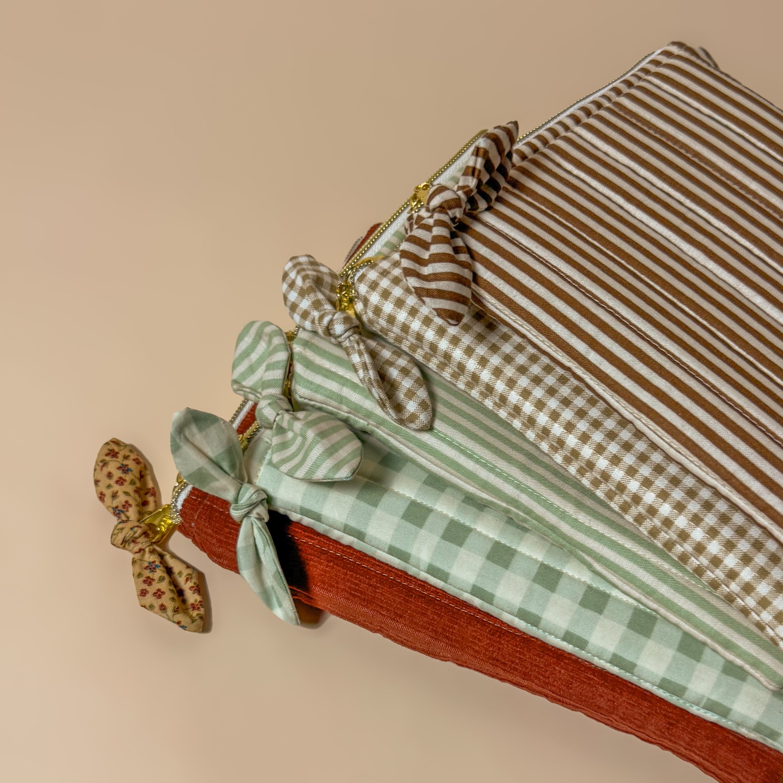 A collection of five handmade quilted Kindle sleeves with zipper closures and decorative bows, featuring patterns like brown stripe, sage green gingham, and red corduroy for stylish e-reader protection.