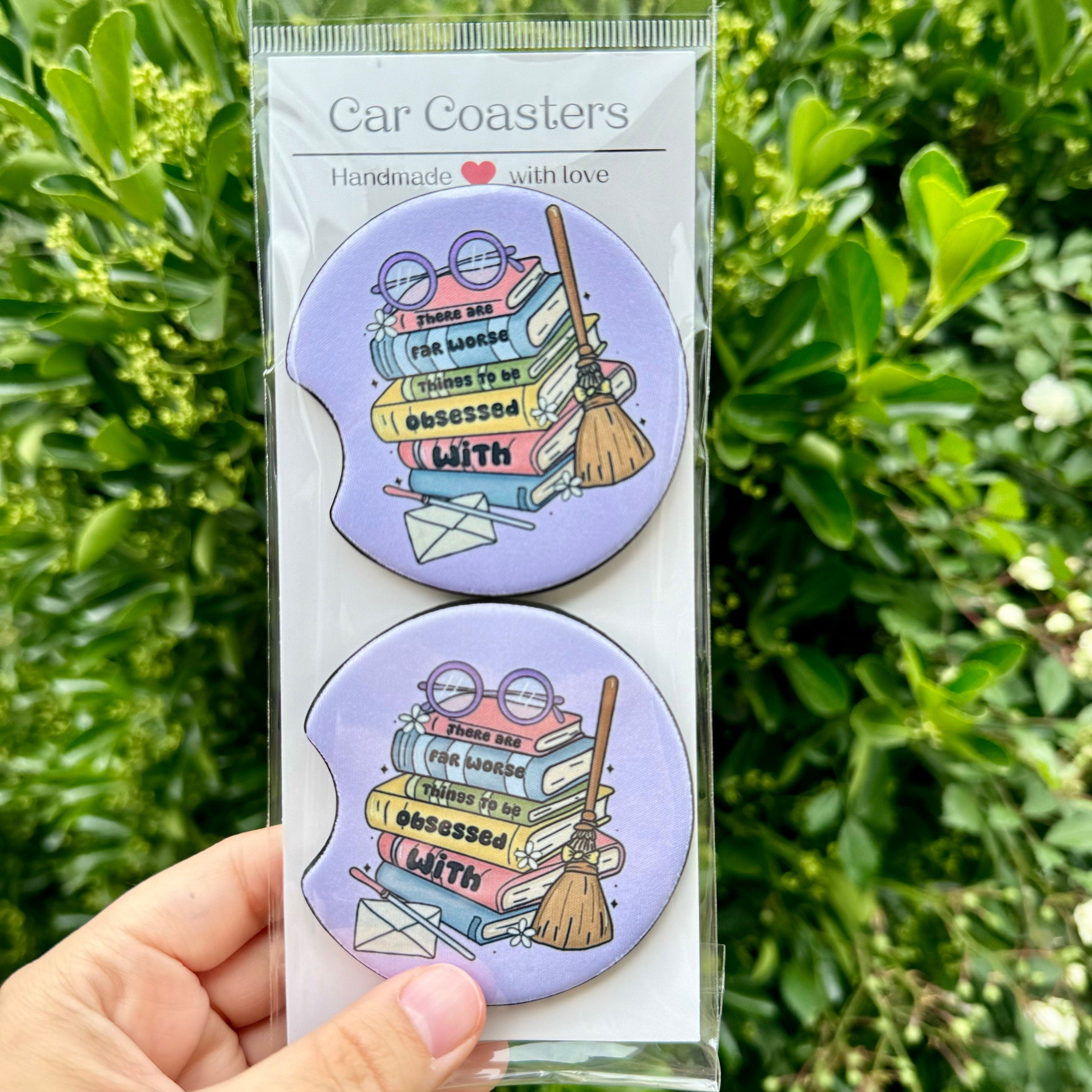 "A 2-pack of purple Stack of Books car coasters by Dex Avenue, featuring a whimsical book stack with the quote 'There are far worse things to be obsessed with,' styled in clear packaging.