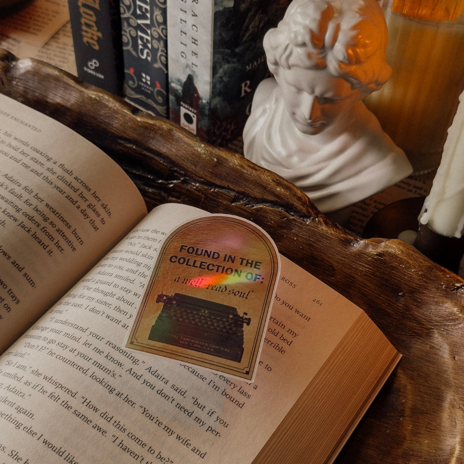 Close-up detail of a holographic "Found in the Collection of: a well-read soul" typewriter sticker on an open book, showcasing the rainbow shimmer in a Dark Academia setting.