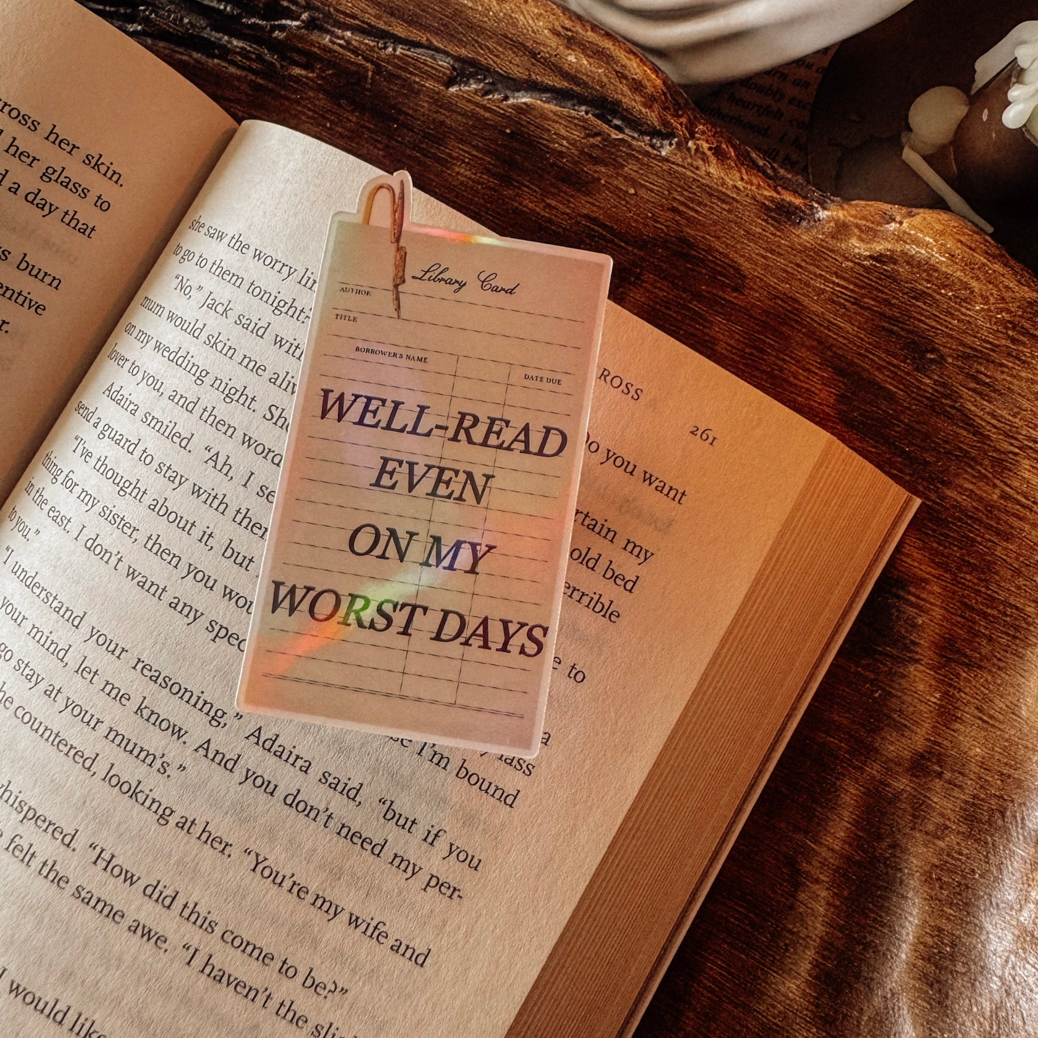 Holographic "Well-Read Even on My Worst Days" sticker on an open vintage book, featuring an ornate frame in a moody Dark Academia setting.