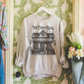 The Curly Quill When the Moon Hatched Sweatshirt in ash grey, styled on a hanger against a vintage floral background